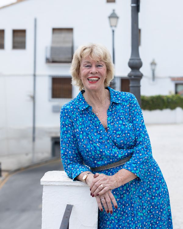 Jessica Larive leunt ontspannen tegen een wit muurtje in een straat in Altea